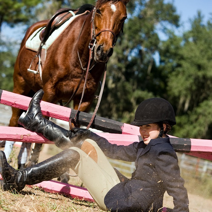 Young female equestrian falls off horse while trying to clear an obstacle in competition
